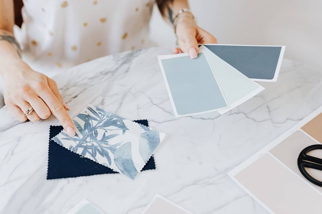 A designer choosing between blue paint chips and a botanical fabric swatch on a marble desk