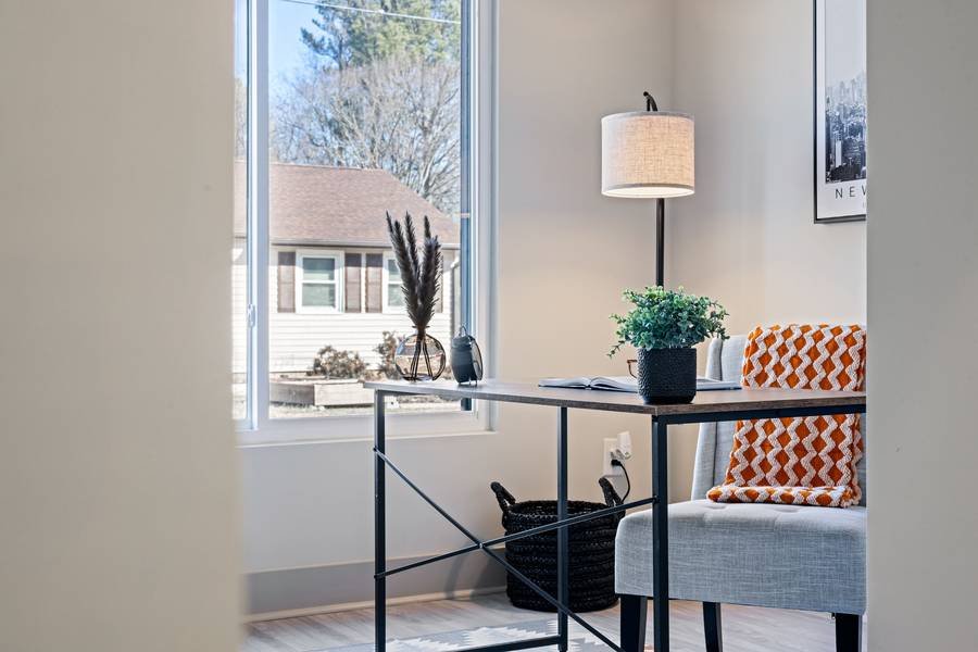 A calm home office with a slim desk by a window, a linen lamp and a patterned chair