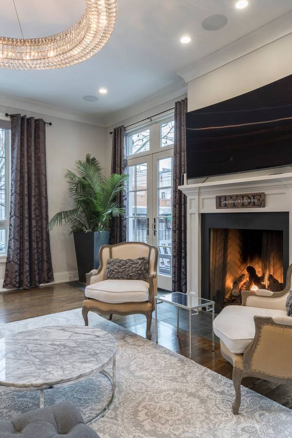 A classic living room styled around a white marble fireplace, with a French armchair and tall windows