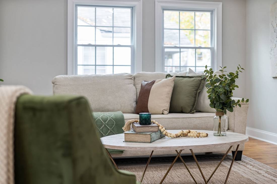 A staged living room with a cream sofa, green velvet chair and a round marble coffee table