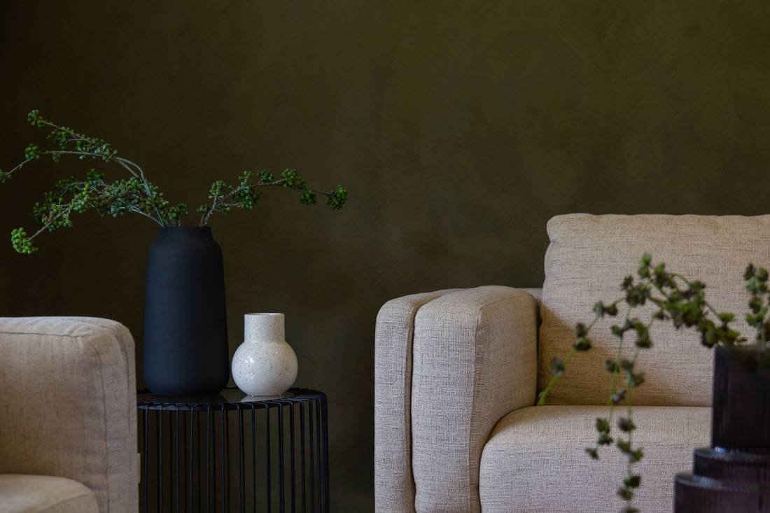 Two cream bouclé armchairs and dark vases against a deep olive wall