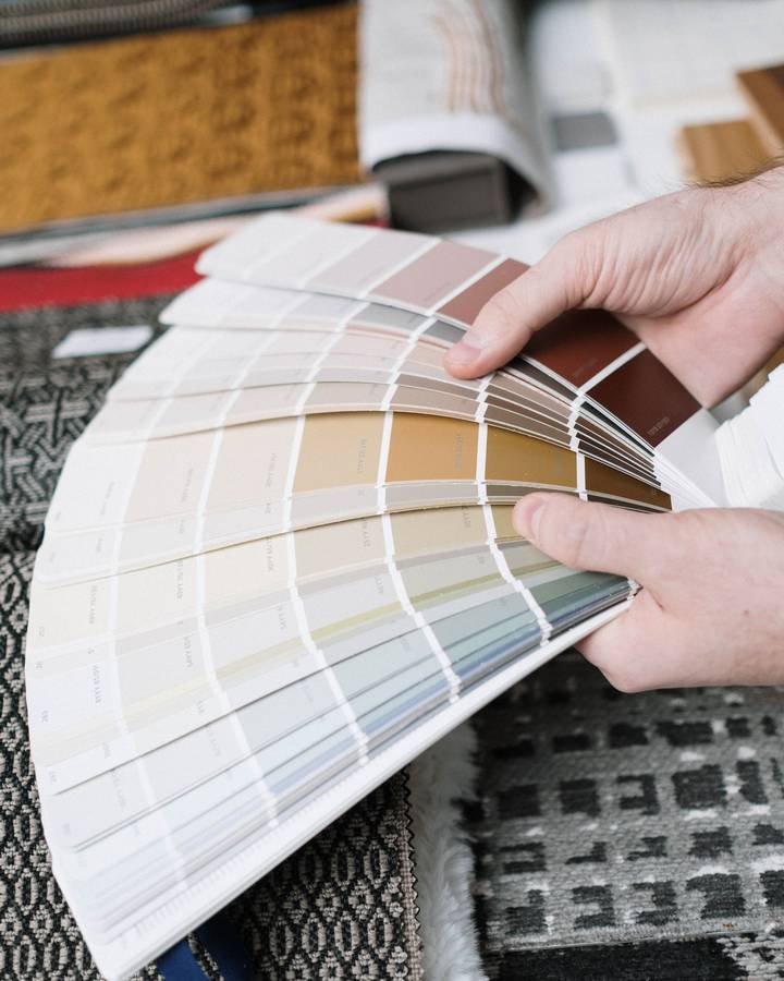 Hands holding a fan deck of warm neutral paint colours over fabric samples