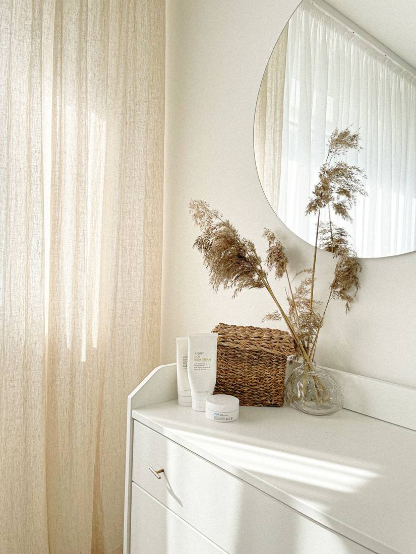 Sheer linen curtains, a round mirror and dried pampas on a white console