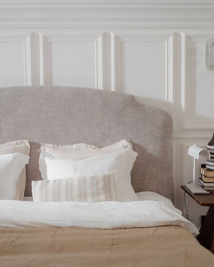 A guest bedroom with a soft upholstered headboard, white bedding and moulded wall panels
