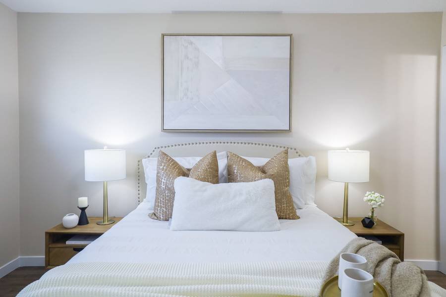 A neutral staged bedroom with matching lamps, layered cushions and abstract art