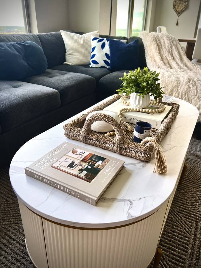 A white oval coffee table styled with a woven tray, a plant and design books