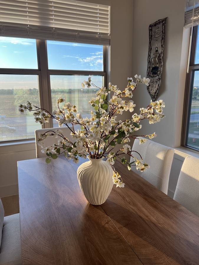 A walnut dining table styled with a fluted white vase of blossom branches in evening light
