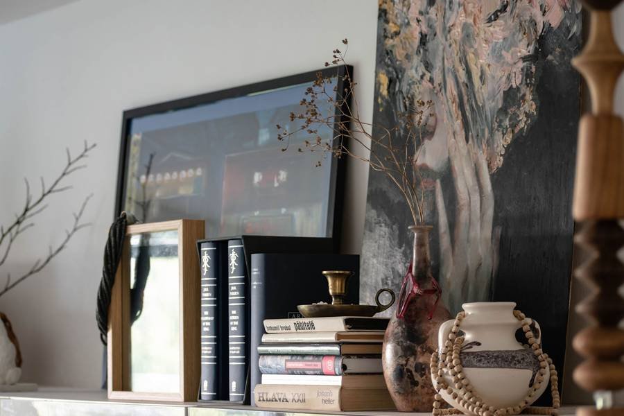 A styled mantel with leaning art, stacked books, a branch and pottery